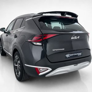 Rear three-quarter view of a dark gray Kia Sportage SUV with red taillights and a roof spoiler in a studio setting