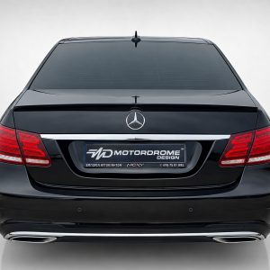 Rear view of a black Mercedes-Benz with red taillights and chrome trim, license plate area displaying a MOTORODROME DESIGN plate.