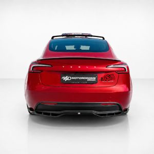 Rear view of a red Tesla in a studio, featuring aftermarket decals on the trunk and a custom plate, spoiler, and dual taillights.