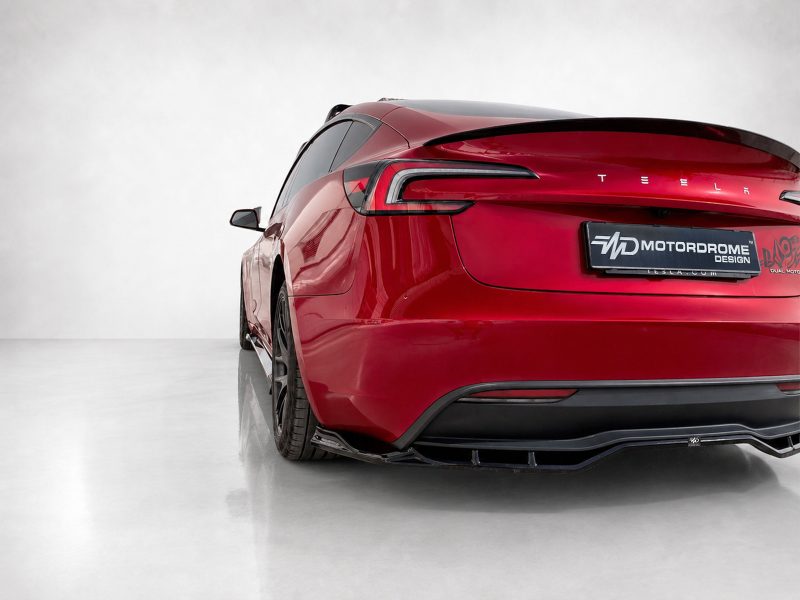 Red Tesla rear quarter view in a clean studio setting, showing taillights and a Motordrome Design plate on the back.