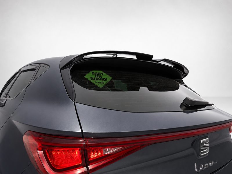 Gray SUV rear with roof spoiler and a green 'BABY ON BOARD' sticker on the rear window