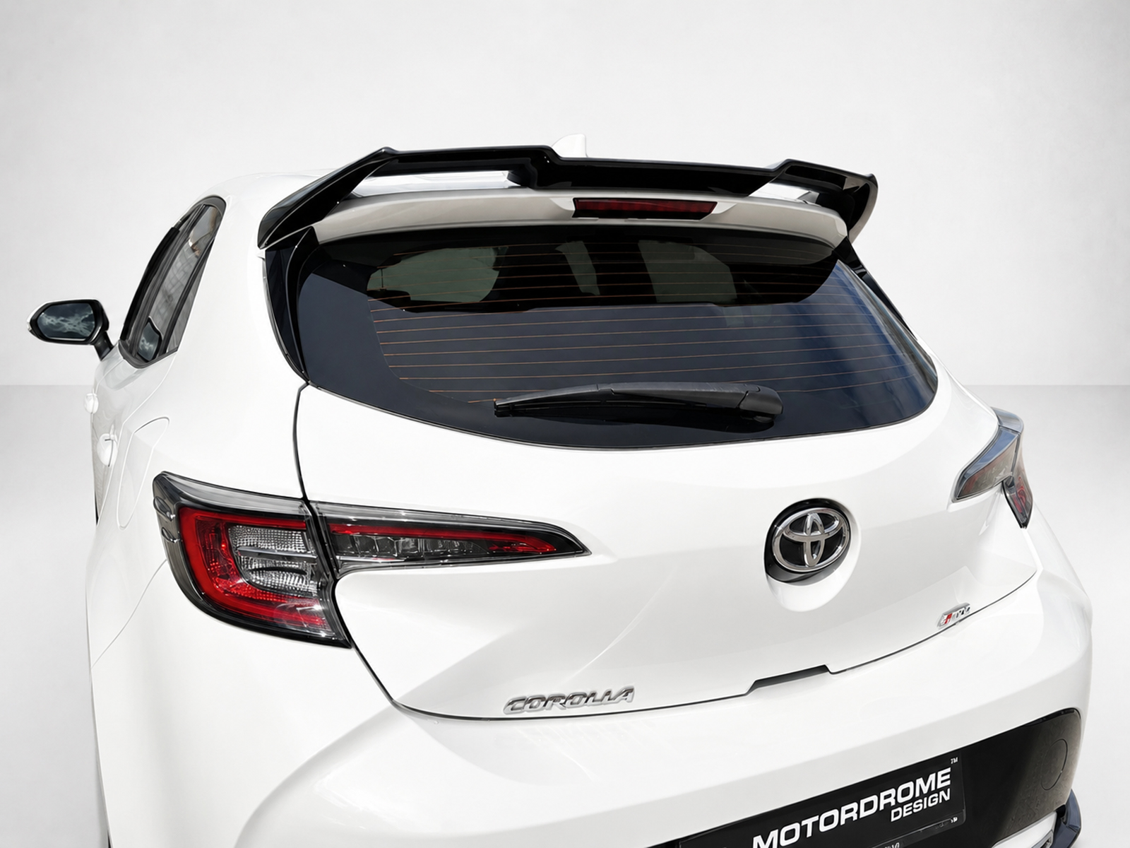 A-511_1jpg - OPSHOLDERS White Toyota hatchback rear view with a large black spoiler, visible rear windshield wiper, and red taillights against a light background