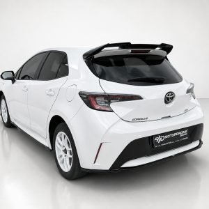 A-511_2jpg - OPSHOLDERS Rear three-quarter view of a white Toyota Corolla hatchback in a studio setting, front wheels turned slightly left with a spoilered roofline visible.
