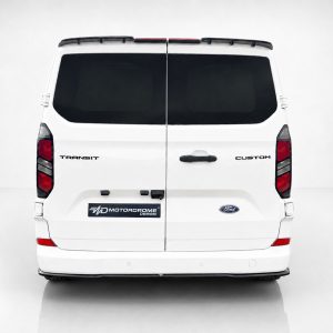 Rear view of a white Ford Transit Custom van with split doors, dark rear windows, and a Motordrome Design plate on the bumper area.”,