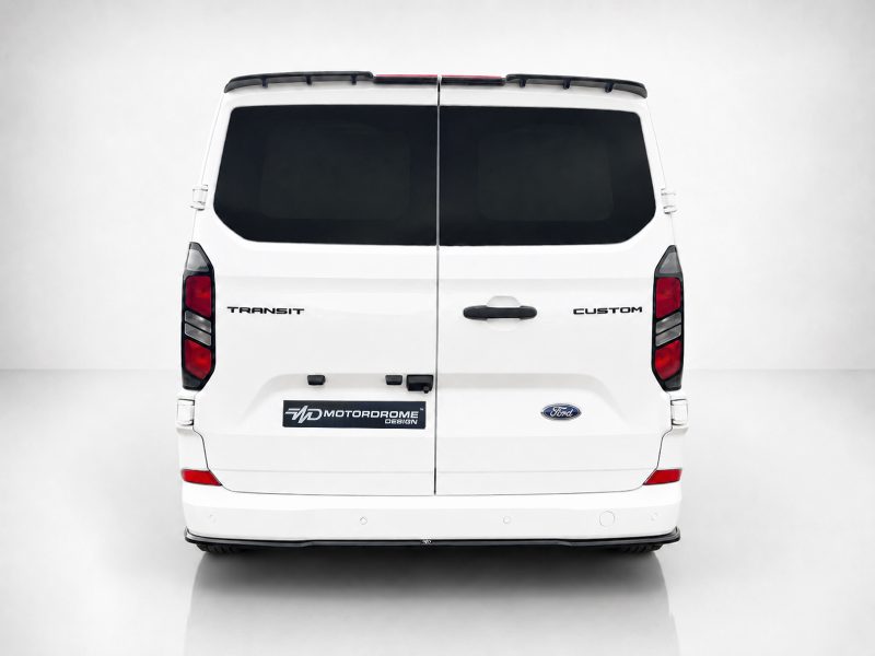 Rear view of a white Ford Transit Custom van with split doors, dark rear windows, and a Motordrome Design plate on the bumper area.”,