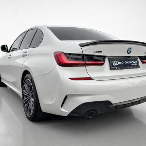 White BMW sedan shown from the rear-right, highlighting sleek taillights, rear bumper, and a black spoiler in a clean studio setting.