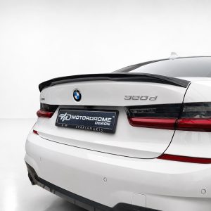Rear view of a white BMW 320d with a black spoiler and red taillights, showcasing a Motordrome Design plate label on the bumper
