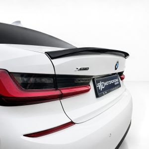 Rear of a white BMW with a black spoiler, red taillights, and an XDrive badge on the trunk lid.