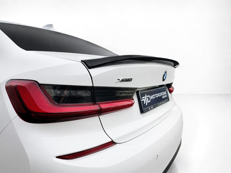 Rear of a white BMW with a black spoiler, red taillights, and an XDrive badge on the trunk lid.