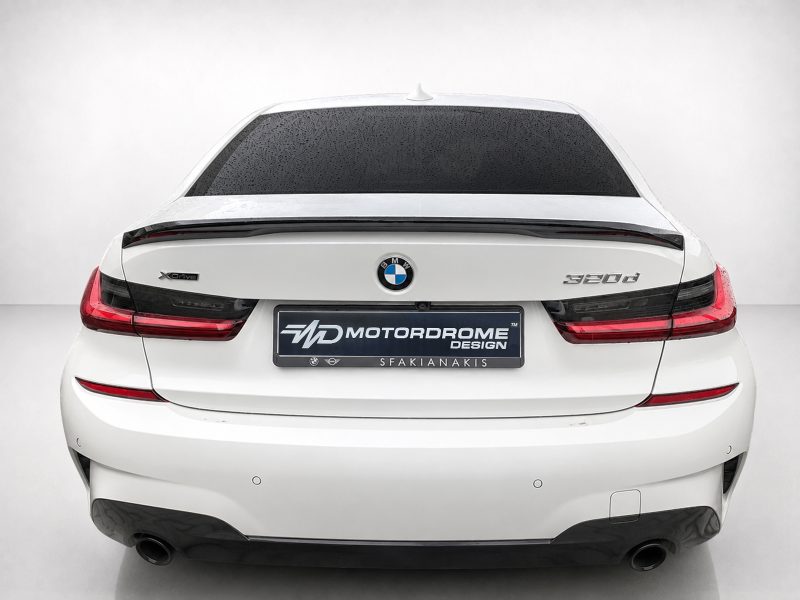 Rear view of a white BMW 520d with a dark rear windscreen and red taillights, displaying a MOTOR DROME DESIGN plate on the trunk.