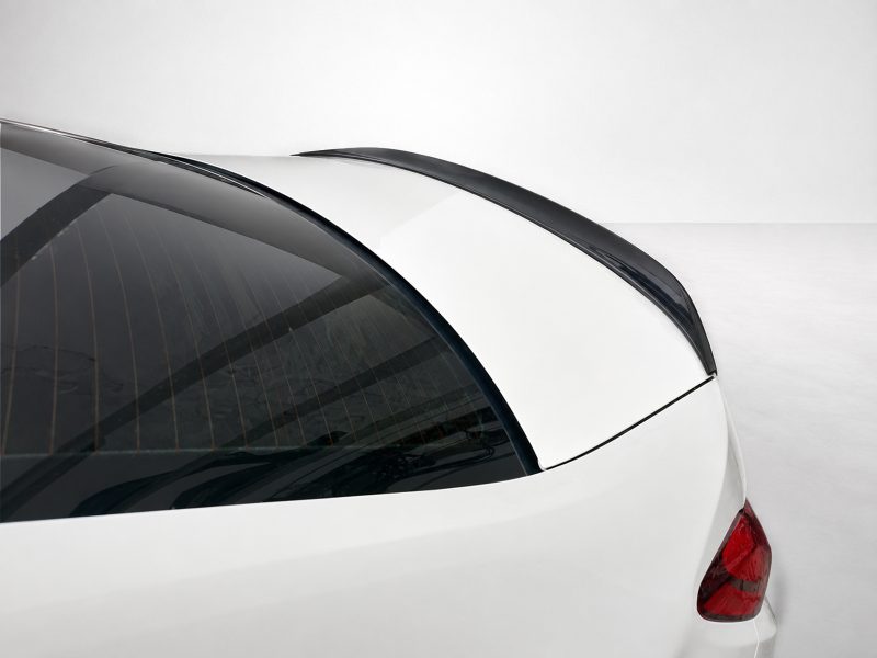 Close-up of a white car's rear end, showing the curved rear window with defroster lines and a black roof spoiler.