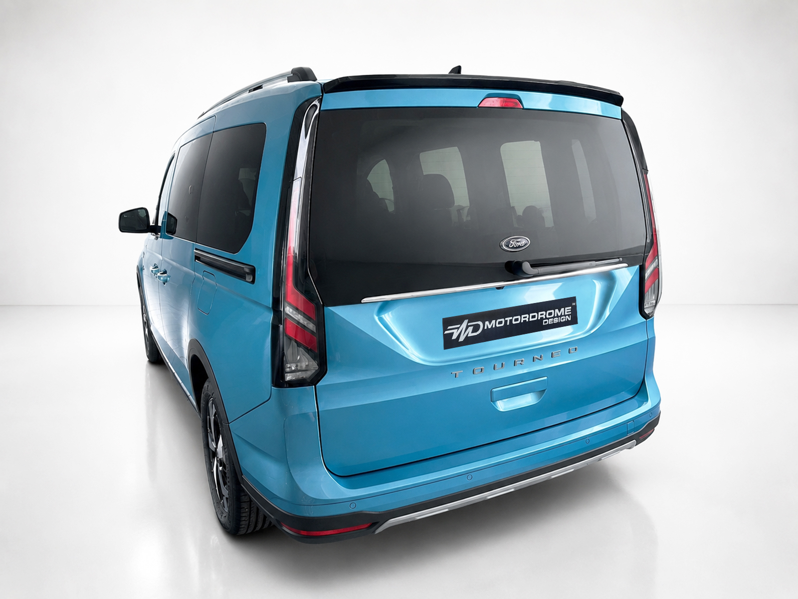 A-516_2jpg - OPSHOLDERS Blue Ford Tourneo van shown from rear three-quarter view in a bright studio setting, blue finish with black rear window and chrome accents, 'MOTORODROME DESIGN' badge visible on tail