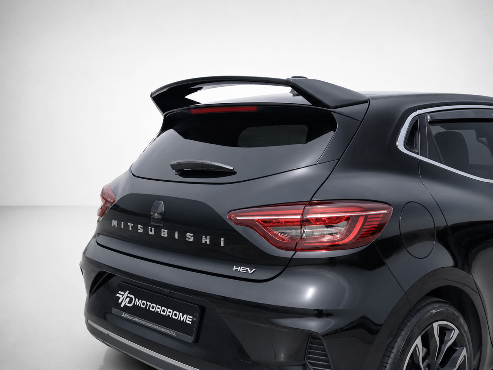 A-520_1jpg - OPSHOLDERS Rear view of a black Mitsubishi SUV/hatchback with a prominent sporty spoiler, red taillights, and HEV badge in a studio setting.