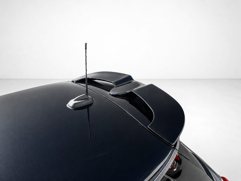 Close-up of a glossy black car roof featuring a slim antenna and a subtle rear spoiler against a light background.