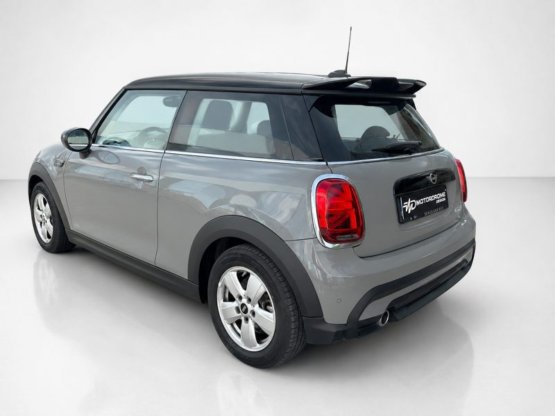Grey Mini Cooper rear three-quarter view with black roof and red taillights in a studio setting