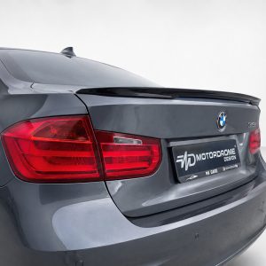 Rear view of a gray BMW with a small trunk spoiler and red taillights, showcasing the brand emblem and a license plate reading MOTORPROME DESIGN (car showroom pose)