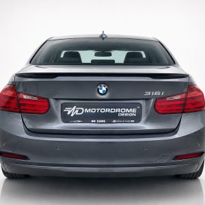 Rear view of a gray BMW 316i with red tail lights and a custom MotorDrome Design plate on the trunk