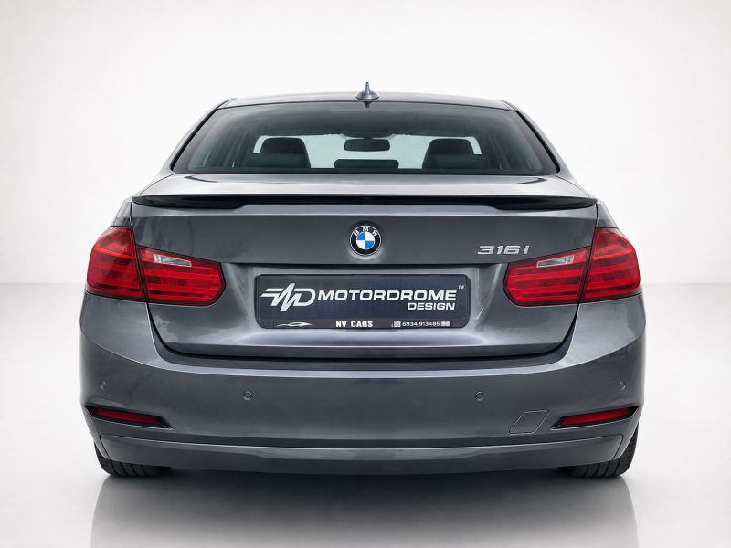 Rear view of a gray BMW 316i with red tail lights and a custom MotorDrome Design plate on the trunk