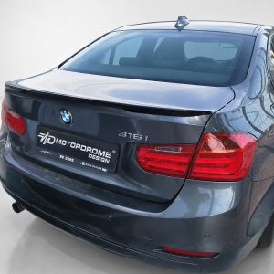 Rear view of a dark blue BMW 316i sedan in a studio, showing the BMW badge, 316i emblem, tail lights, and a Motordrome Design dealership plate