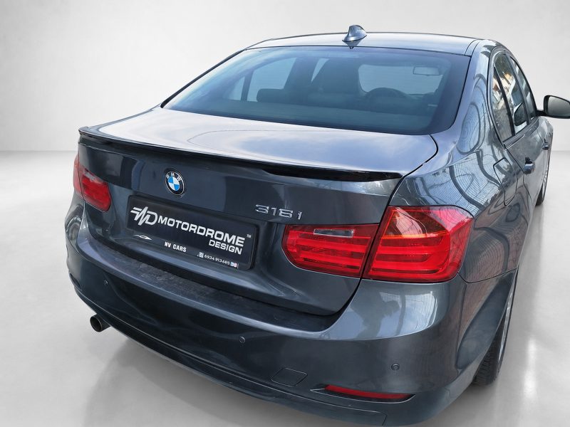 Rear view of a dark blue BMW 316i sedan in a studio, showing the BMW badge, 316i emblem, tail lights, and a Motordrome Design dealership plate