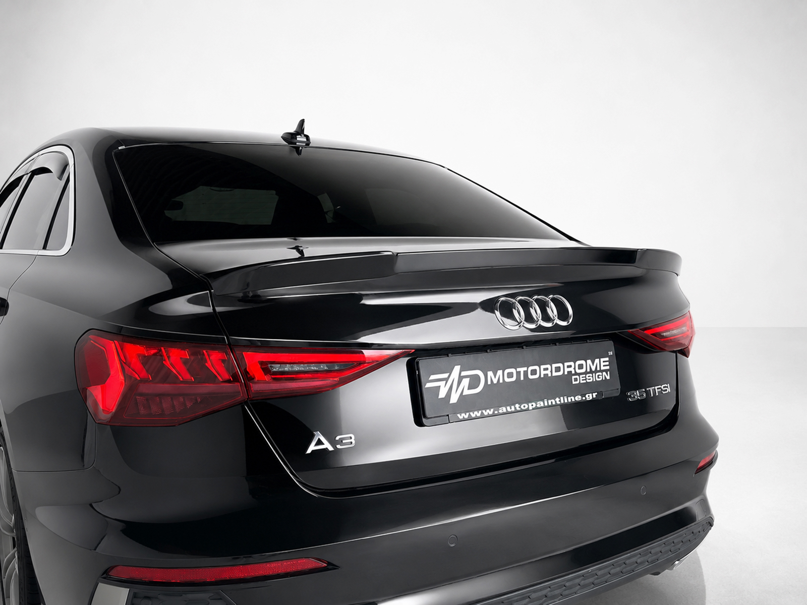 A-529_1jpg - OPSHOLDERS Rear view of a sleek black Audi A3, showing the taillights and trunk with a branded license plate reading MOTORDROME DESIGN