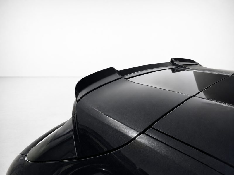 Close-up of a glossy black sports car rear roof with an integrated spoiler against a white studio backdrop.