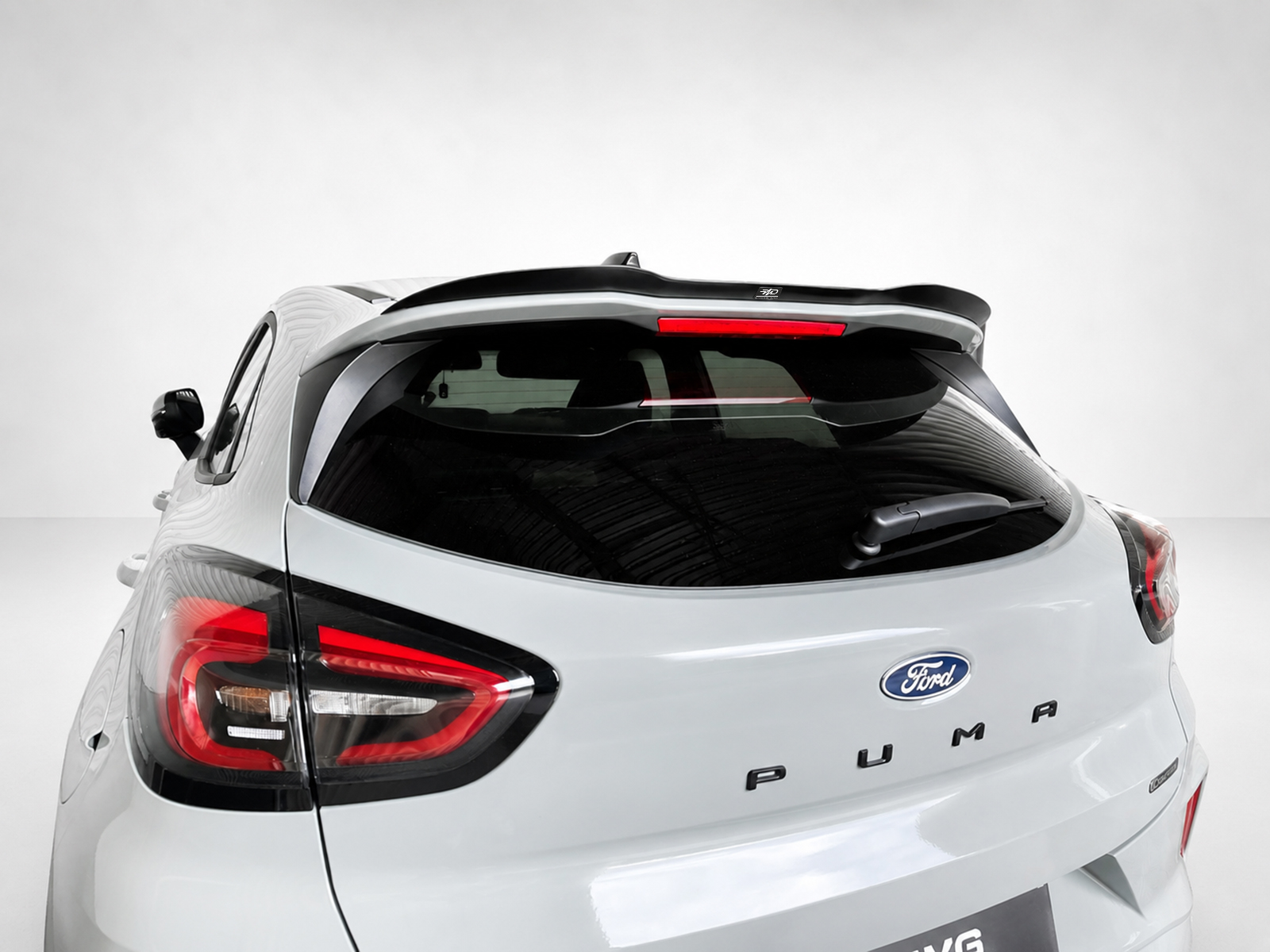 A-531_1jpg - OPSHOLDERS Rear three-quarter view of a white Ford Puma, showing taillights, rear wiper, and roof spoiler (car model and branding visible).