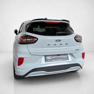 A-531_2jpg - OPSHOLDERS Rear view of a light blue Ford Puma SUV in a studio setting, showing taillights, Ford badge, and rear bumper detail.