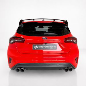 Rear view of a bright red Ford hatchback with a spoiler, black rear window, and four exhaust tips in a studio setting; Motordrome Design plate visible on the tailgate.