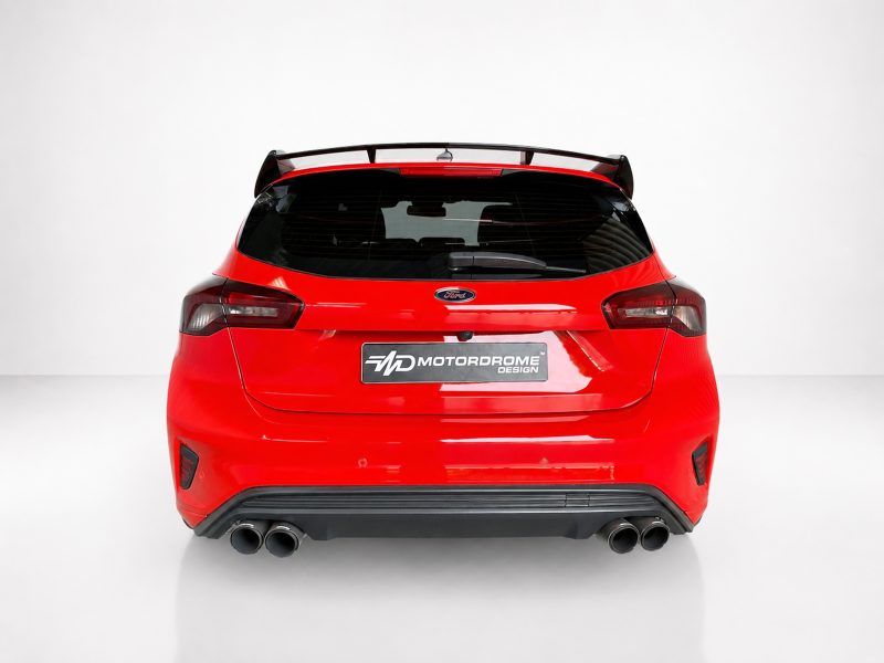 Rear view of a bright red Ford hatchback with a spoiler, black rear window, and four exhaust tips in a studio setting; Motordrome Design plate visible on the tailgate.