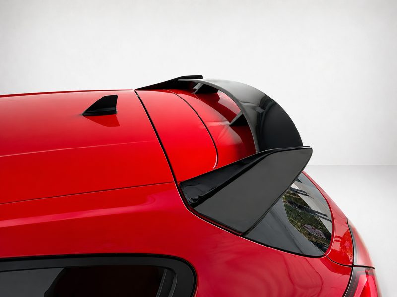 Close-up of a red car's roof showing a rear spoiler, shark-fin antenna, and rear window.