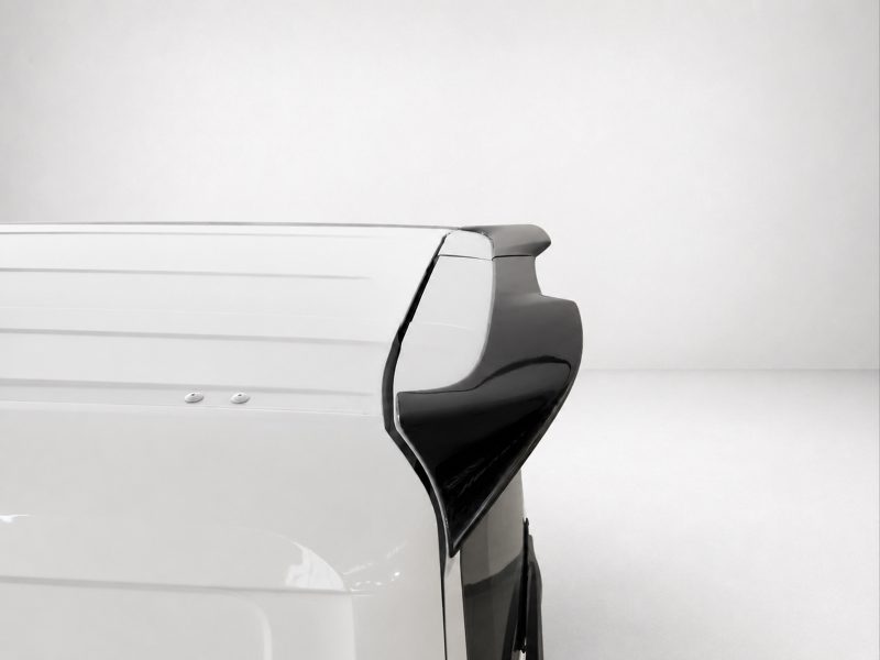 Rear right corner of a white van with a black rear spoiler against a plain light background.