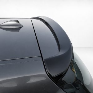 Close-up of a dark gray car roof with a curved rear spoiler and a small roof fin against a light background.