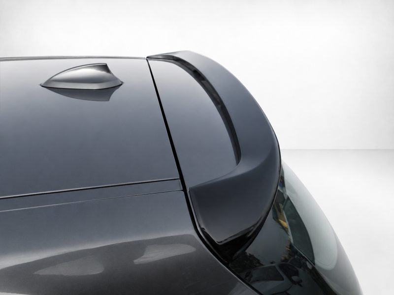 Close-up of a dark gray car roof with a curved rear spoiler and a small roof fin against a light background.