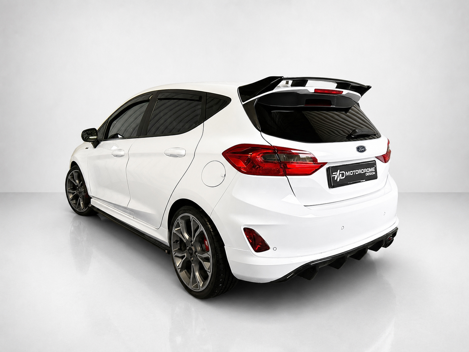 A-535_2jpg - OPSHOLDERS White modified hatchback viewed from the rear-quarter, featuring a large wing, dark-tinted windows, and custom alloy wheels in a studio setting.