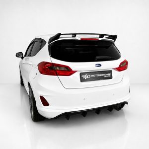A-535_6jpg - OPSHOLDERS Rear three-quarter view of a white Ford hatchback with a black spoiler and 'MotorDrome' plate in a bright studio setting.
