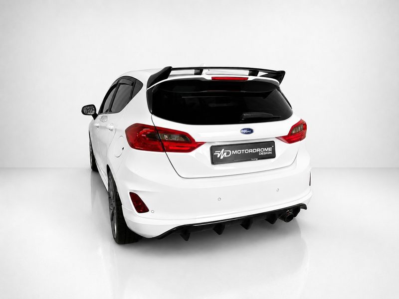 A-535_6jpg - OPSHOLDERS Rear three-quarter view of a white Ford hatchback with a black spoiler and 'MotorDrome' plate in a bright studio setting.