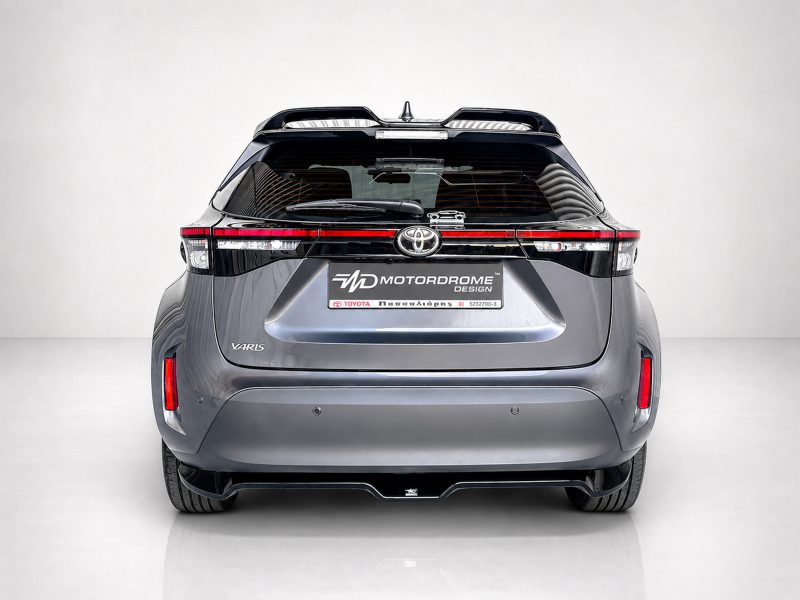 A-536_3jpg - OPSHOLDERS Rear view of a metallic gray Toyota Yaris in a studio, showing the tail lights and a MD Motordrome Design plate on the hatch.