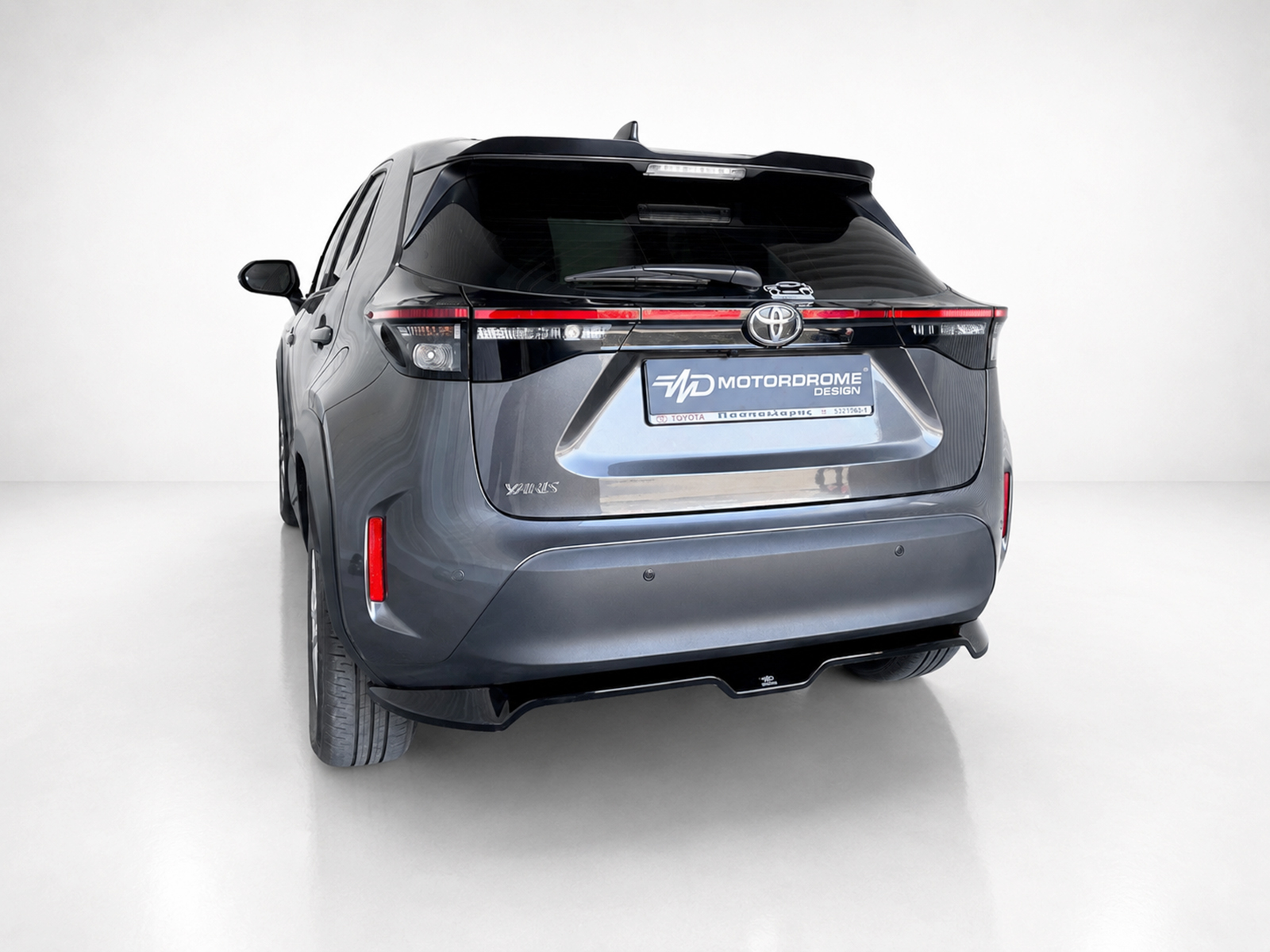 A-537_1jpg - OPSHOLDERS Rear view of a dark gray Toyota SUV in a studio setting, showing taillights, rear bumper, and license plate area with a 'Motordrome' plate cover
