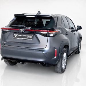 A-537_3jpg - OPSHOLDERS Rear three-quarter view of a blue-gray Toyota Yaris SUV in a studio, showing prominent taillights and a Motordrome Design plate.