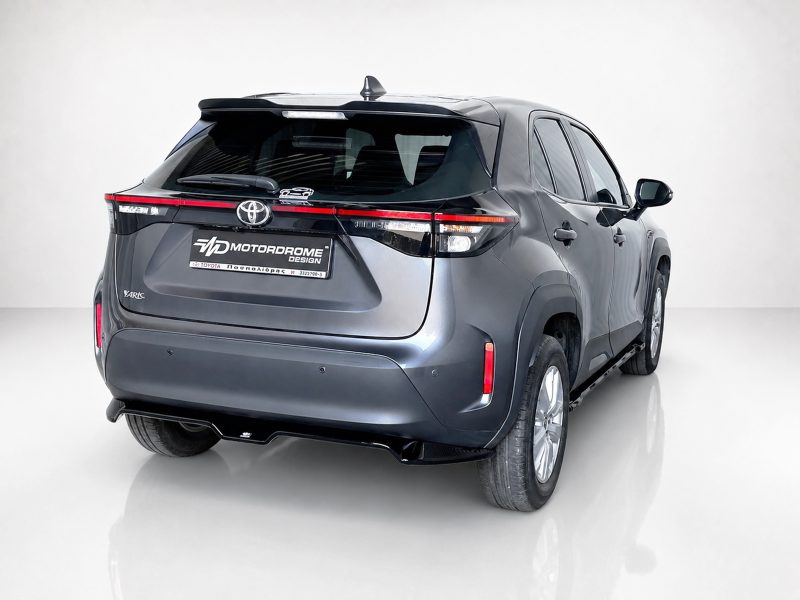 A-537_3jpg - OPSHOLDERS Rear three-quarter view of a blue-gray Toyota Yaris SUV in a studio, showing prominent taillights and a Motordrome Design plate.