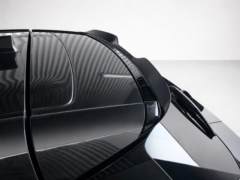 A-537_4jpg - OPSHOLDERS Close-up of a glossy black car with curved panels and a windshield wiper resting on the glass, highlighting reflections and sleek design.