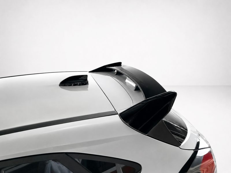 A-538_4jpg - OPSHOLDERS Close-up of a white car's rear with a black spoiler extending over the trunk area against a light gray background