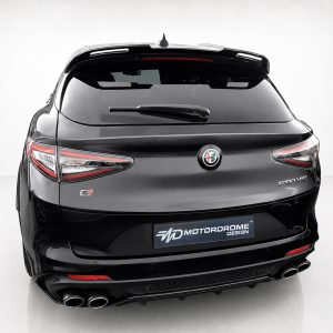 Rear view of a black Alfa Romeo Stelvio SUV in a studio setting, showing distinctive taillights, badge, and dual exhausts with a MotorDrome Design plate below the bumper