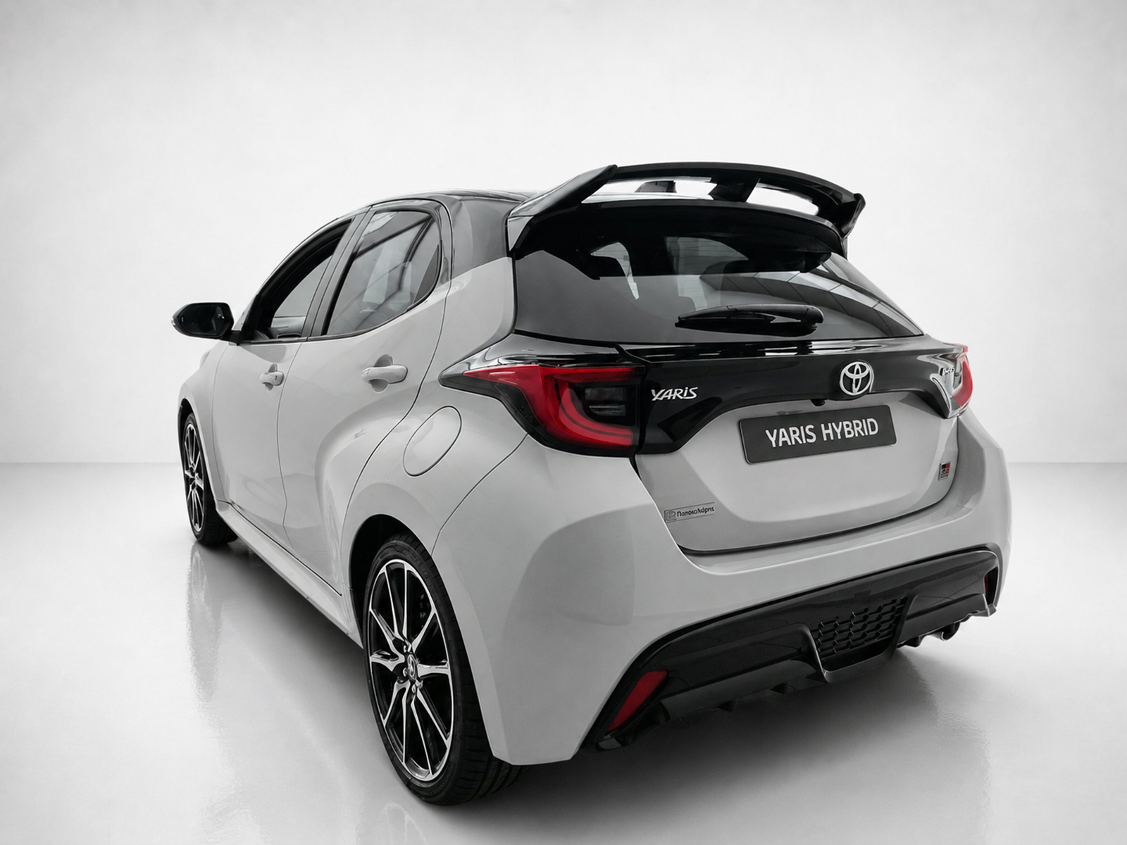 A-541_2jpg - OPSHOLDERS Rear three-quarter view of a white Toyota Yaris Hybrid hatchback in a studio setting with a black roof spoiler