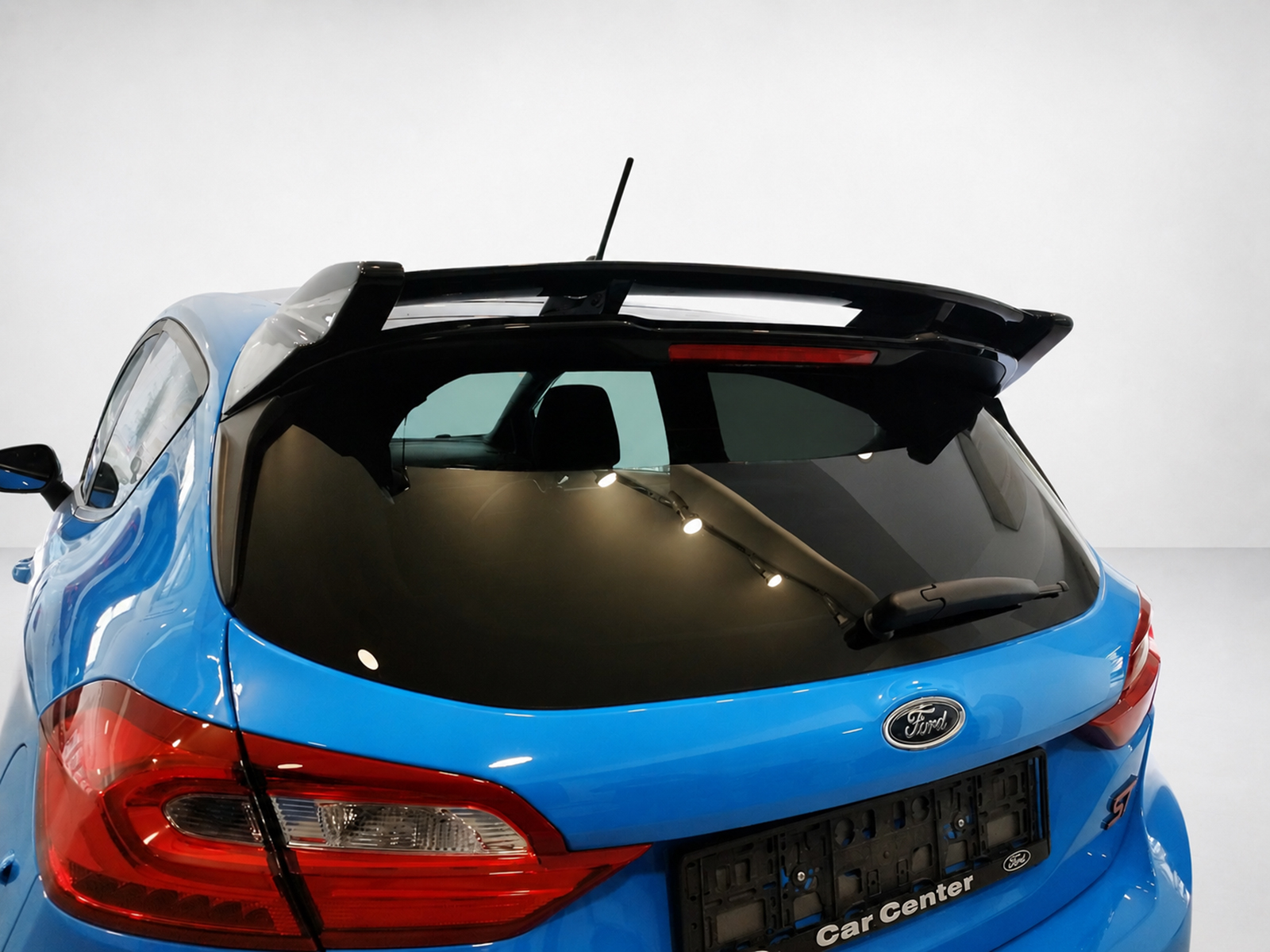 A-542_1jpg - OPSHOLDERS Rear view of a blue Ford hatchback with a dark rear window and roof spoiler in a studio setting