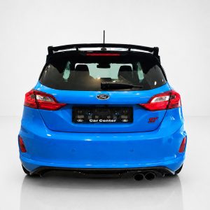 A-542_3jpg - OPSHOLDERS Blue Ford hatchback rear view in a white studio, showing tail lights, rear window, spoiler, and dual exhausts with Car Center plate edge visible.