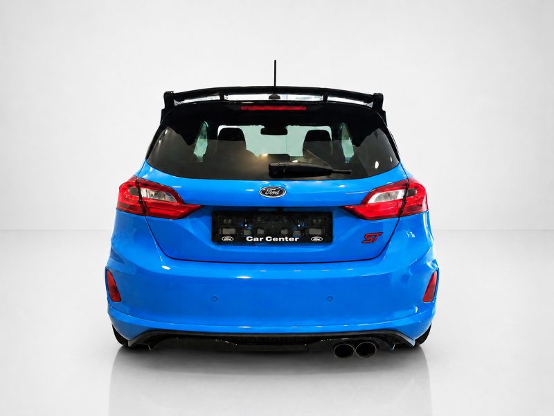 A-542_3jpg - OPSHOLDERS Blue Ford hatchback rear view in a white studio, showing tail lights, rear window, spoiler, and dual exhausts with Car Center plate edge visible.
