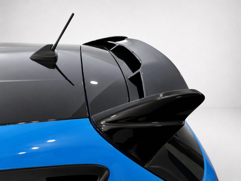 A-542_4jpg - OPSHOLDERS Close-up of a blue car's rear section showing a black spoiler and roof antenna and a light backdrop.