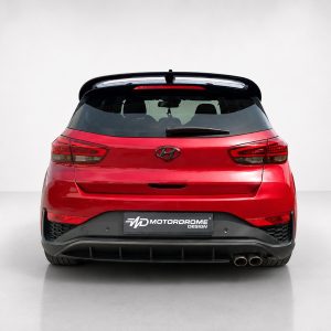 Red Hyundai hatchback rear view in a studio setting with a black spoiler and dual exhausts. Plate reads 'MotorDrome Design'.